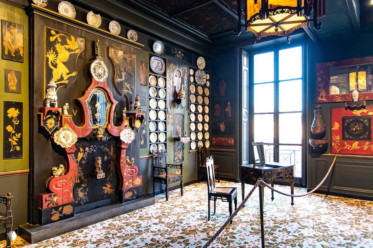 Комната с высоким окном, стульями и коллекцией китайской и европейской декоративной посуды, вид на внутренний интерьер дома Виктора Гюго и экспозицию у окна.