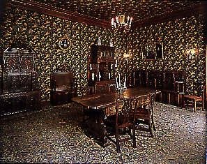 Тёмный угол интерьера с декоративными панелями, мелкими экспонатами и узорчатым ковром — атмосферный фрагмент экспозиции в доме Виктора Гюго.