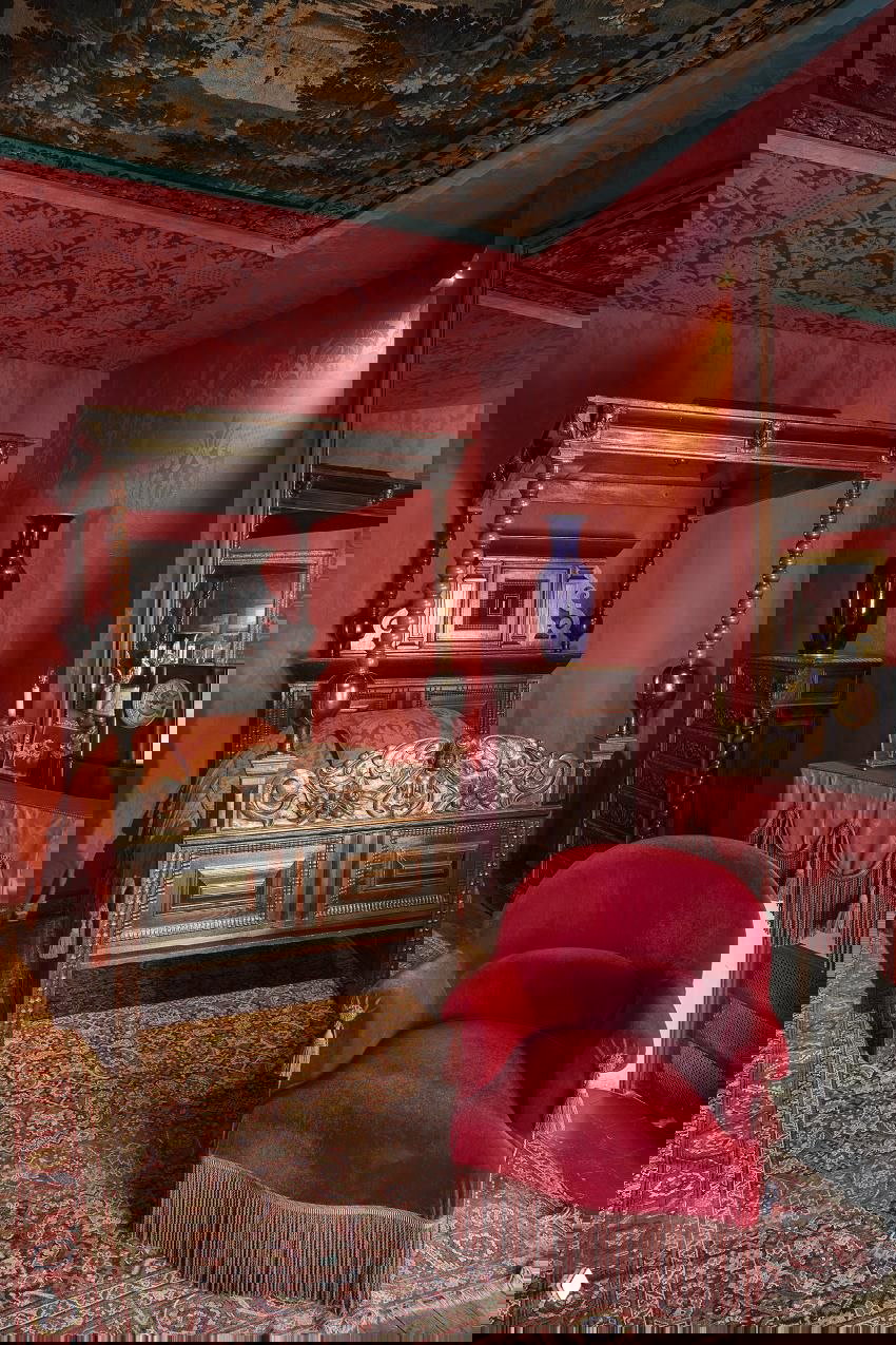 Красная спальня с балдахином, резной деревянной кроватью и бархатным креслом в доме Виктора Гюго — интимный интерьерный фрагмент музейной экспозиции.