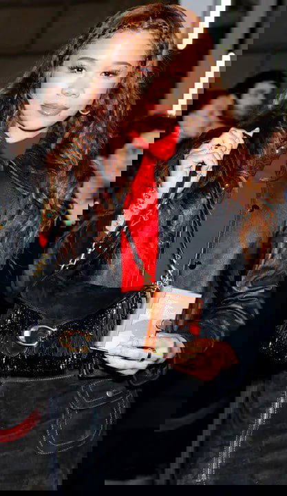 Глянцевый кадр горожанки с сумкой и небольшим книжным аксессуаром в руках, видно оформление обложки и размер подвески.