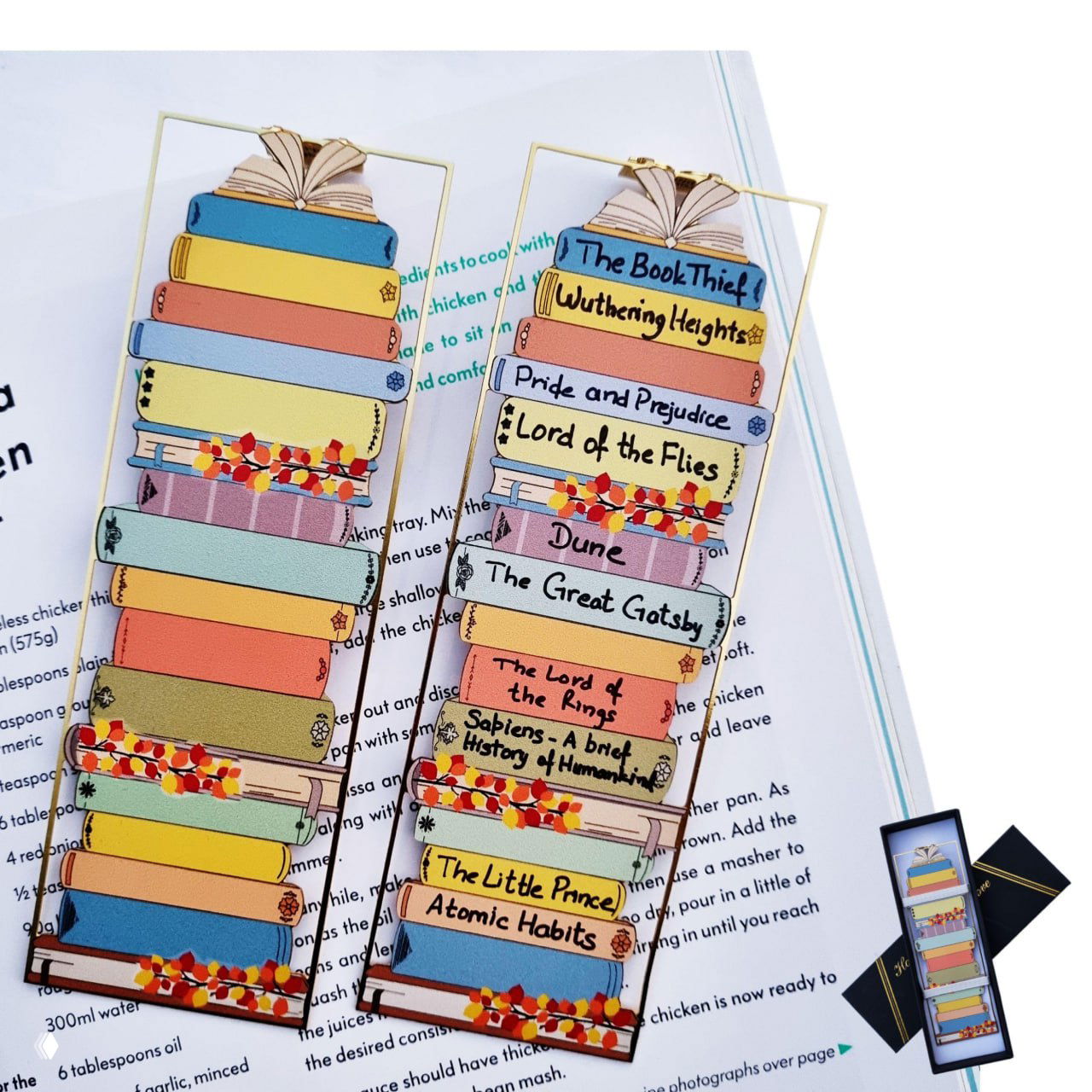 Набор закладок с изображением стопки книг, на корешках написаны названия — декоративные книжные закладки как трекеры прочтения.