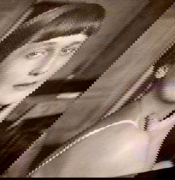 Черно‑белое фото интерьерного портрета: женская фигура в платье и шляпе на фоне картин и мебели, атмосферный антураж времени.