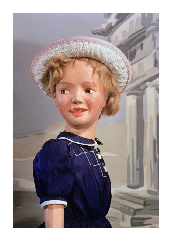 Крупный цветной портрет куклы в синем платье и шляпе: детализированная роспись лица, видна текстура гипса и ткани.