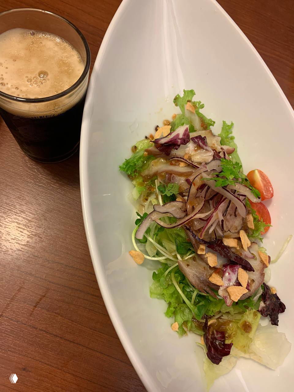 Салат с зеленью, красным луком и кусочками жареного мяса рядом с стаканом тёмного пива — вечерняя атмосфера изакая.