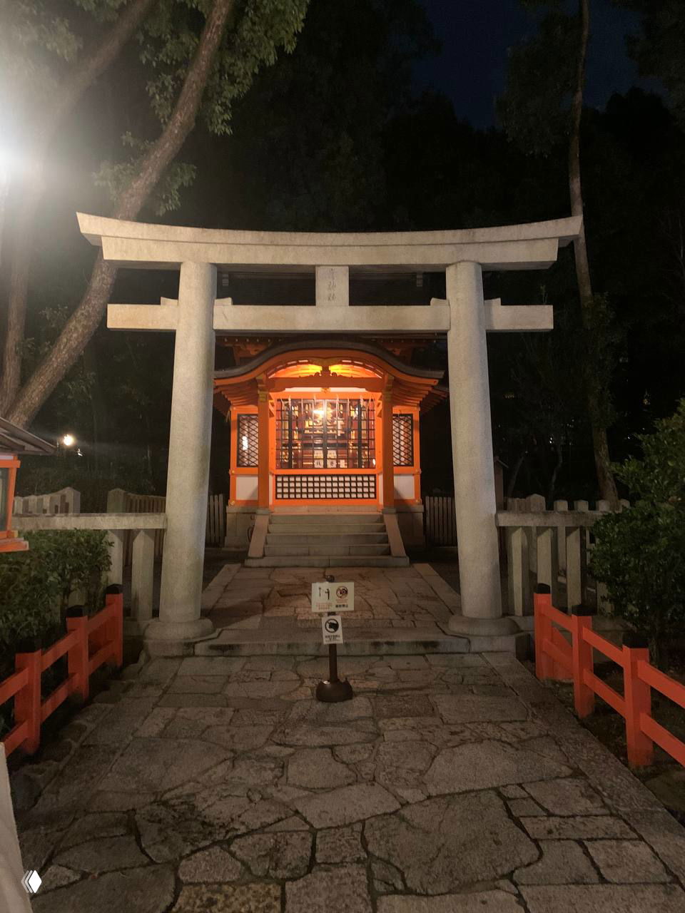 Тёмный тории и небольшой святилищный павильон, подсвеченные ночью; пример городской сцены возле традиционных мест.