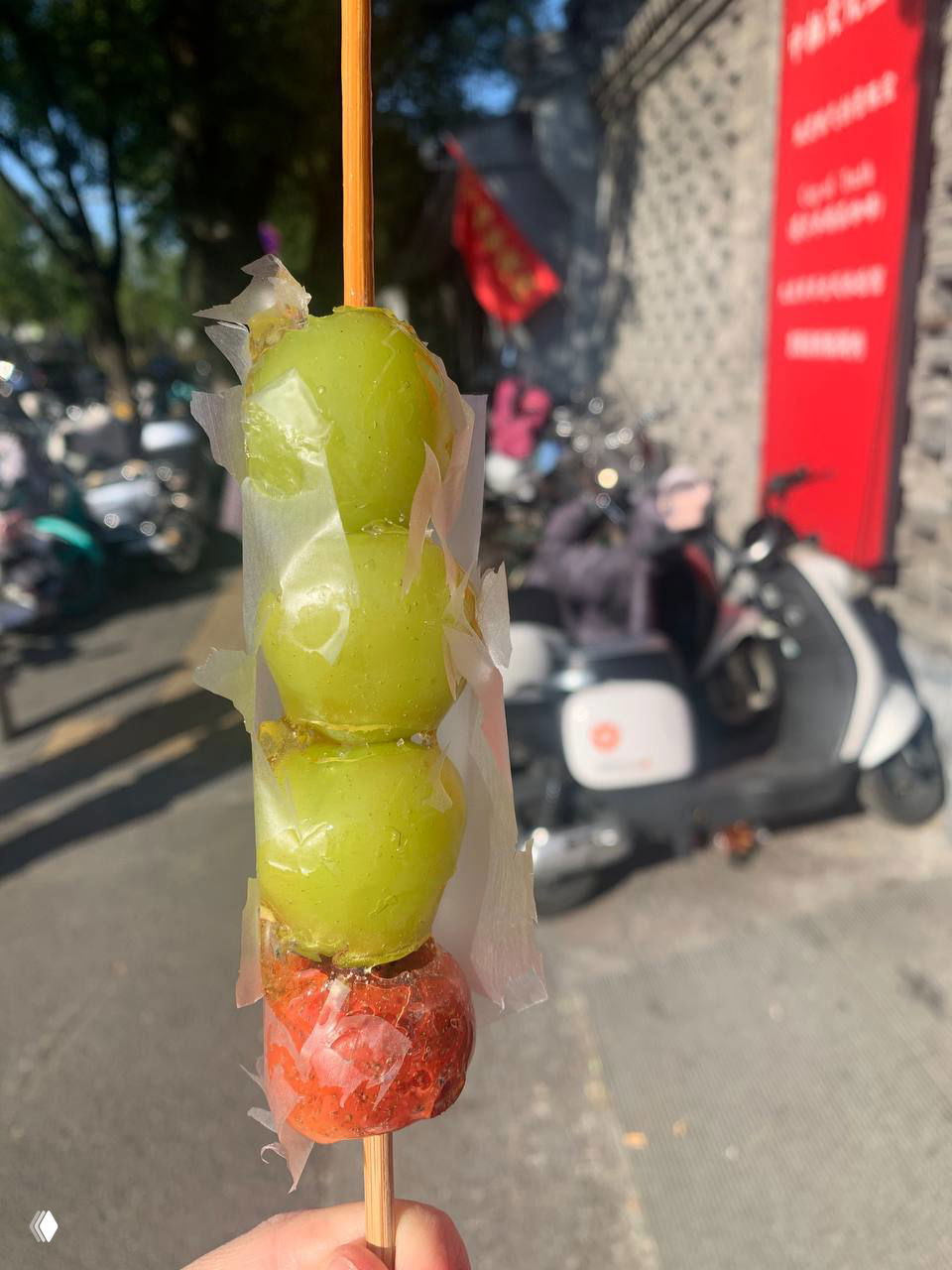 Уличный фуд в Пекине: крупный план засахаренных фруктов на шпажке (тангхулу) в прозрачной глазури на фоне городской улицы.