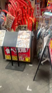 Уличная торговая зона с рекламными стендами, товарами и неоновыми элементами, создающая плотную среду внимания и стремление пройти внутрь заведений.