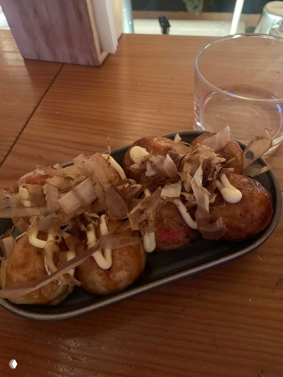 Тарелка такояки — жареные шарики с соусом, майонезом и стружкой бонито на деревянном столе, близкий план в ресторане.