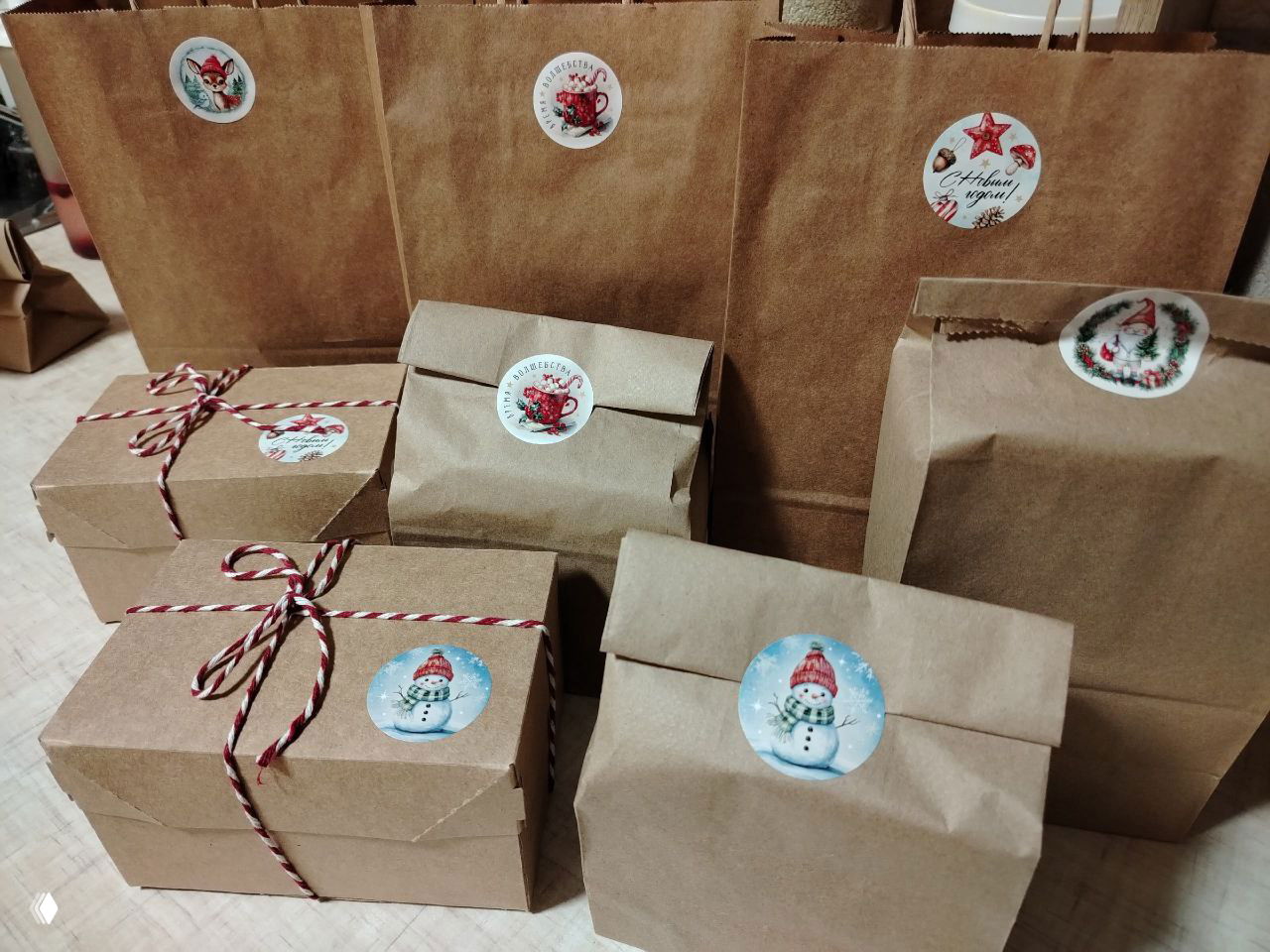 Набор крафт‑пакетов и коробочек с зимними наклейками и мотком бечёвки — упакованные подарки и заказы, готовые к отправке.