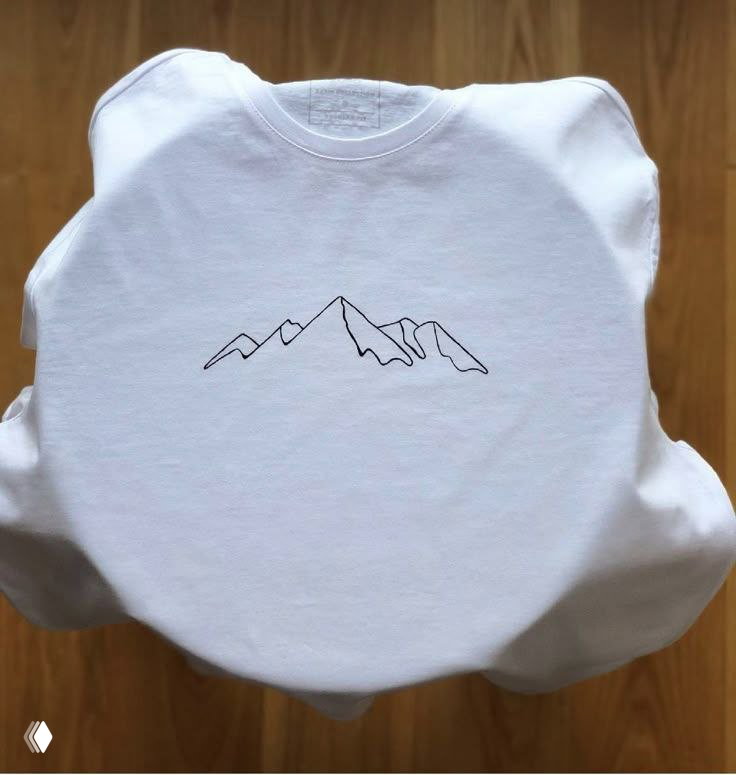 Белая футболка с тонким линейным рисунком горного силуэта в центре, пример нанесения графической вышивки на одежду.