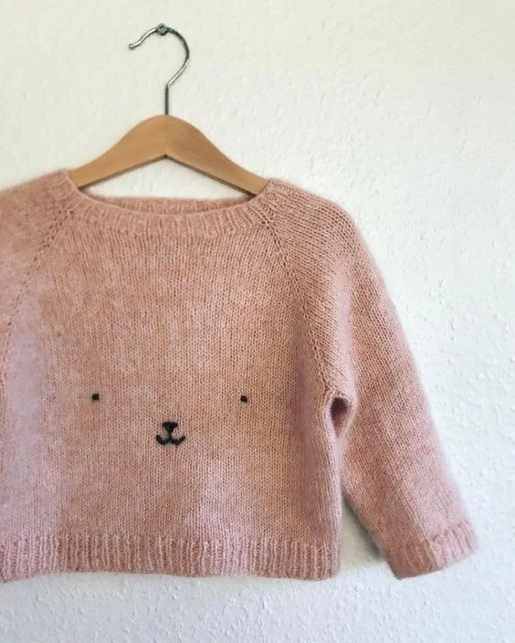 Розовый вязаный свитер на вешалке с минимальным декоративным рисунком — пример одежды, на которую можно наносить вышивку.
