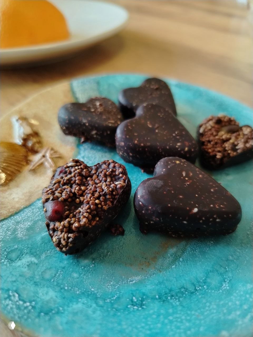 Готовые сердечки из домашнего шоколада с хрустящим попкорном из амаранта и вяленой клюквой на бирюзовой тарелке — финальная подача угощения.