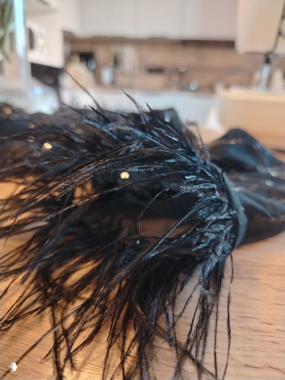 Макросъёмка чёрных перьев и деталей украшения на рабочем столе мастерской; видны нитки, блёстки и фактура перьев в процессе создания.