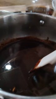 Кастрюля с растопленным какао и силиконовой лопаткой — тёмная гладкая шоколадная масса на водяной бане в процессе перемешивания.