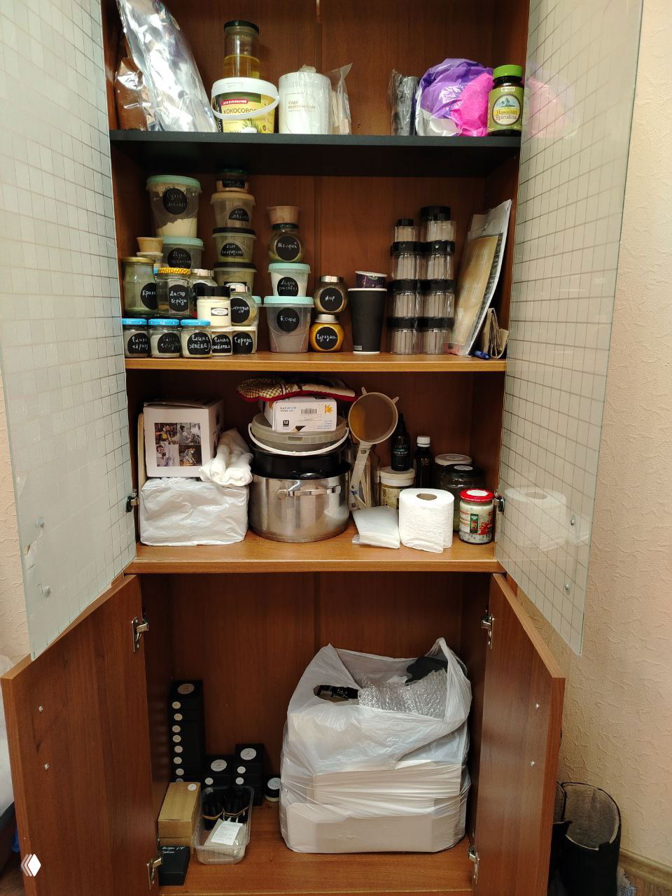 Открытый шкаф в мастерской с аккуратно расставленными баночками и ингредиентами для натуральной косметики.