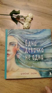 Книга «Одна девочка не одна» лежит на деревянном столе рядом с белыми сухими цветами — общий план, видна обложка и композиция с букетом.
