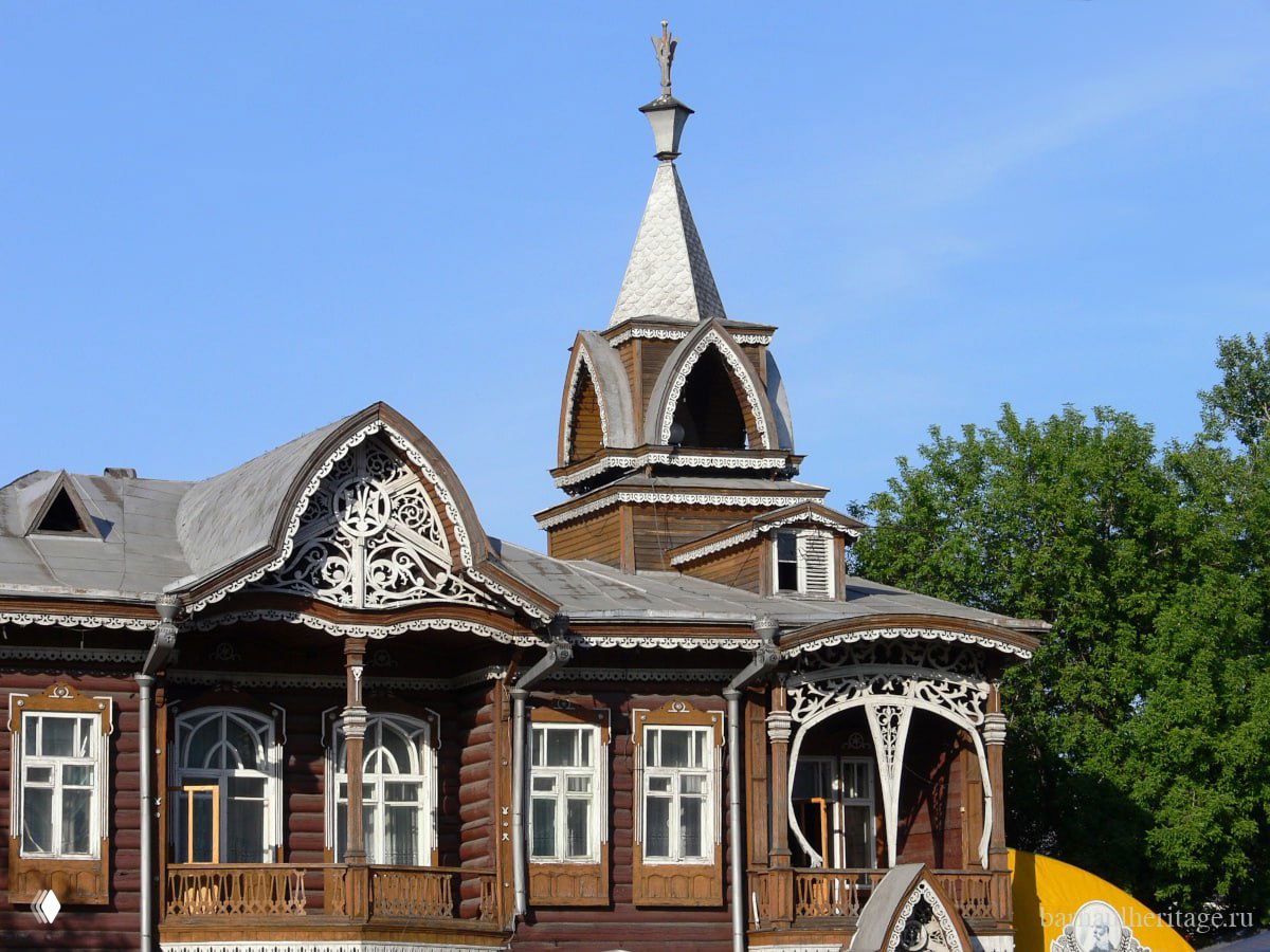 Фрагмент башенки и резных карнизов деревянного дома Шадрина на летнем фоне, крупный план декоративных деталей фасада.