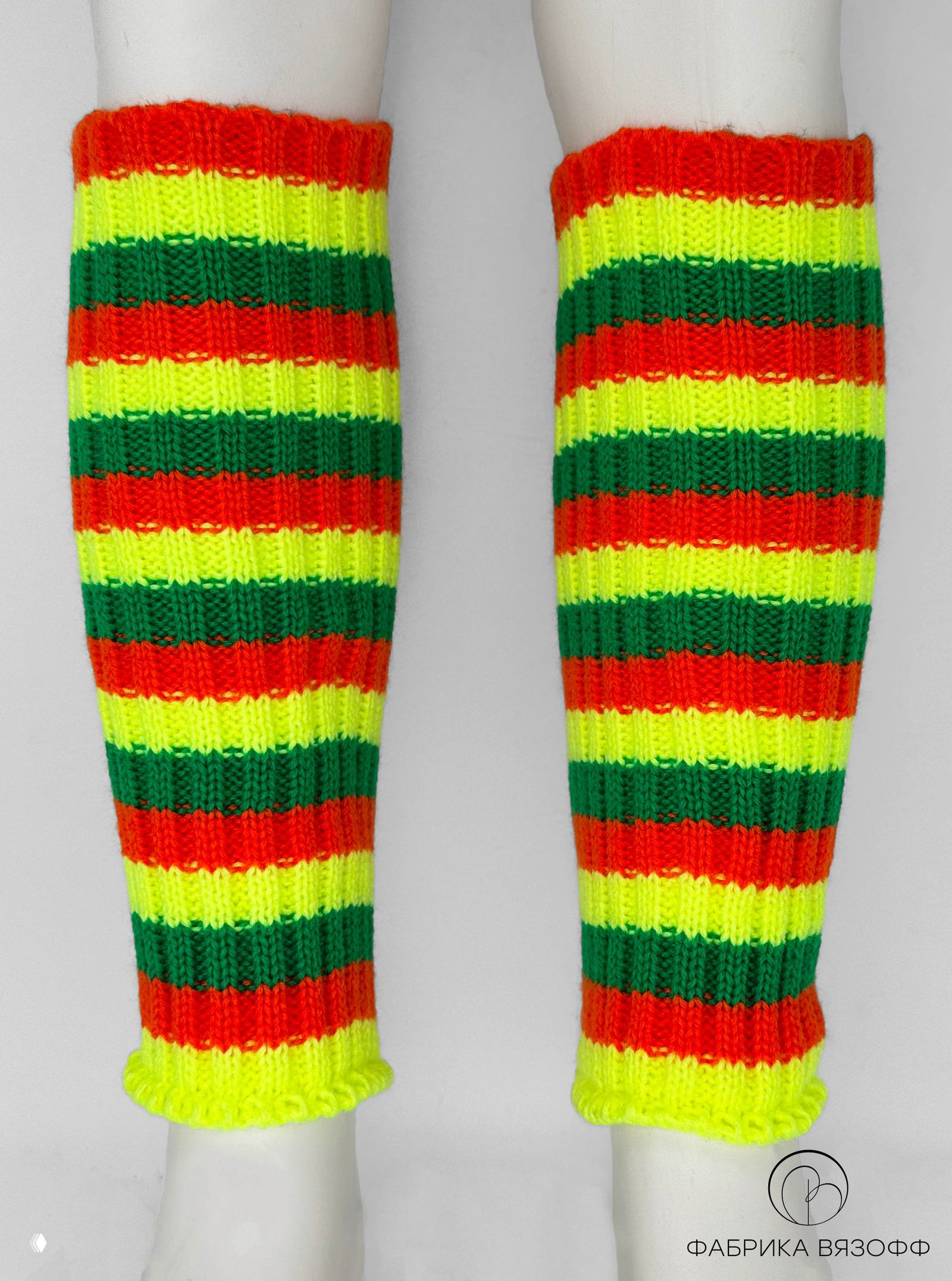Неоново‑жёлто‑зелёно‑оранжевые вязаные гетры в яркую полоску на манекенных ногах; чёткая вязка, контрастные полосы на нейтральном фоне студии.