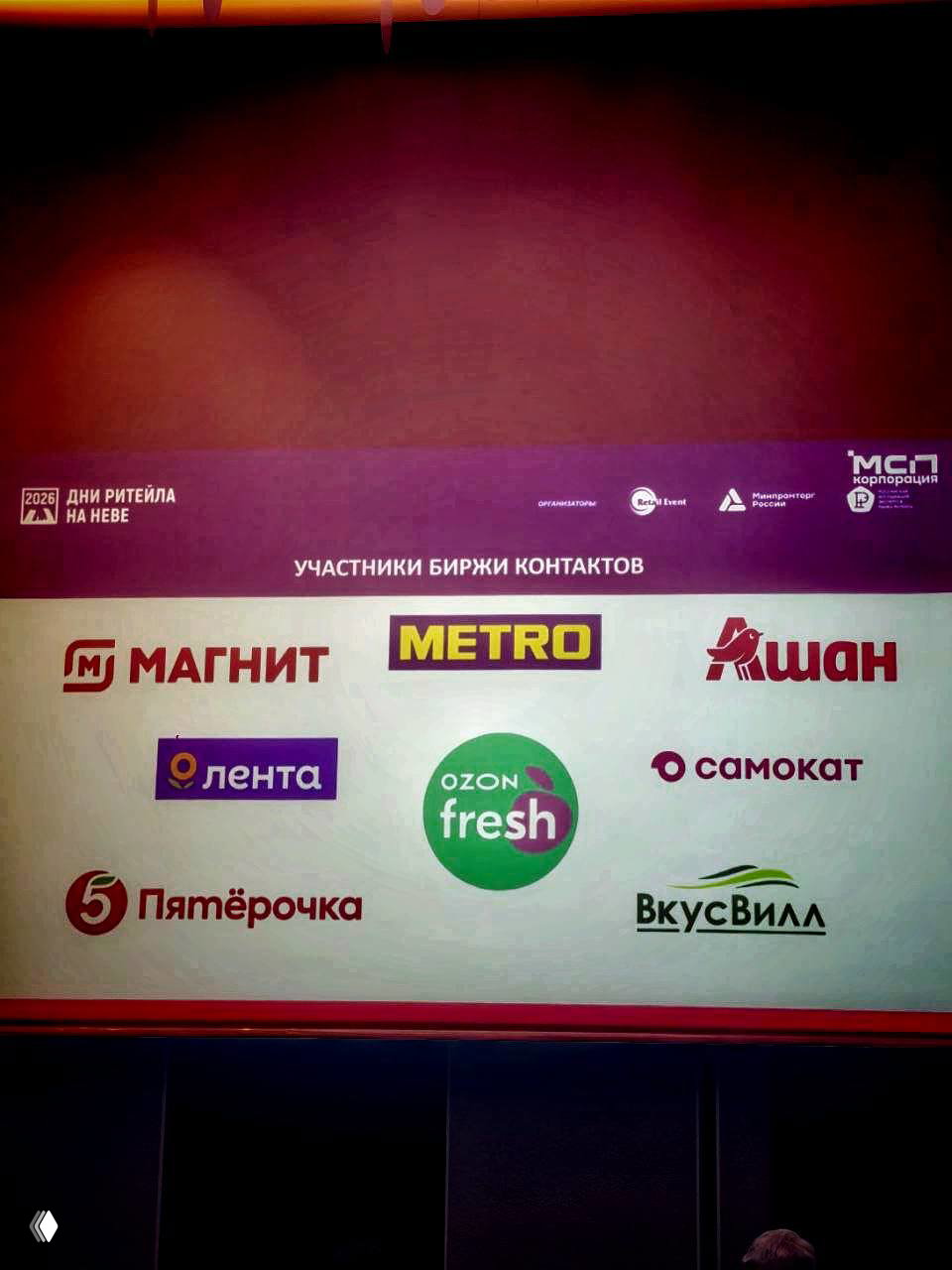 Снимок проектора с логотипами участников биржи контактов: Магнит, Metro, Ашан, Лента, Ozon fresh, Самокат, Пятёрочка, ВкусВилл — список партнёров мероприятия.