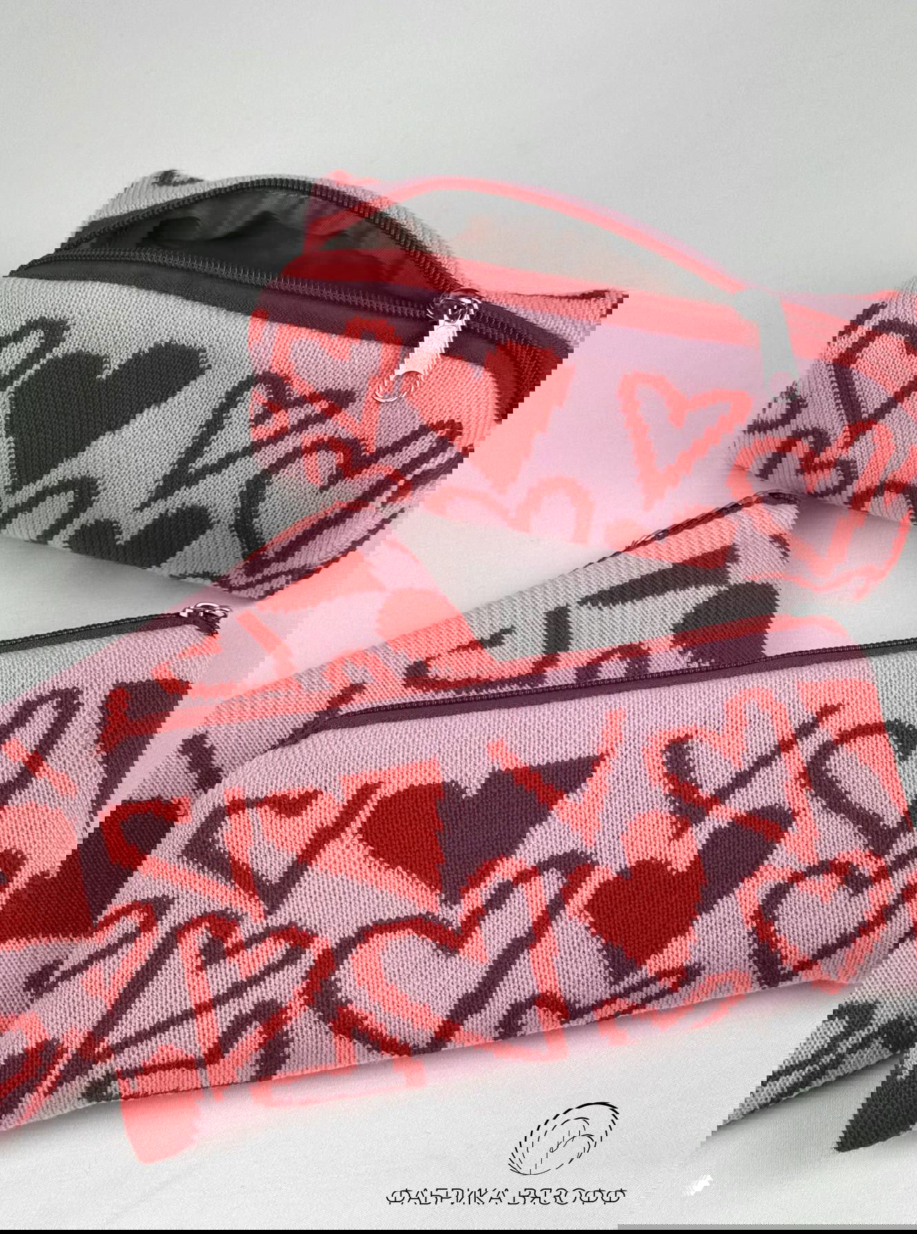 Две вязаные косметички-пеналы розово-красного цвета с принтом сердечки, вид сверху, показана металлическая молния и внутренняя подкладка.