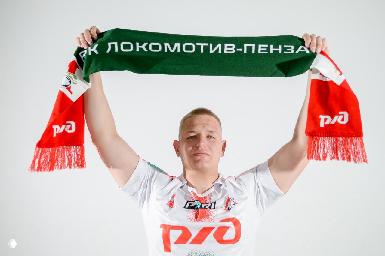 Игрок держит над головой зелёно‑красный шарф с надписью «РК ЛОКОМОТИВ‑ПЕНЗА», демонстрация лицевой стороны вязаного шарфа.