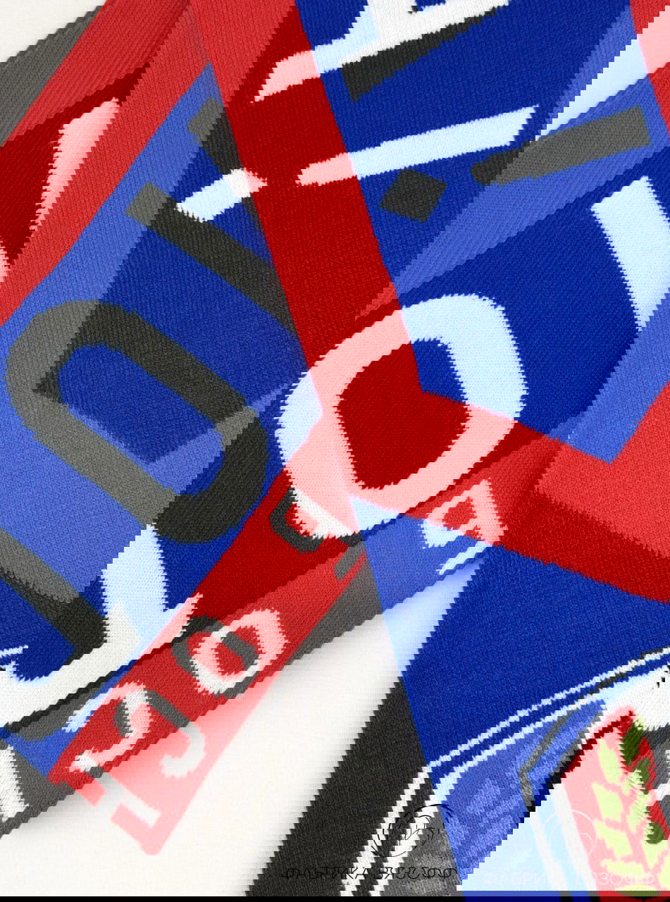 Несколько фрагментов шарфа в синем и красном цвете, виден повтор эмблемы и год «2012», акцент на общей композиции изделия.