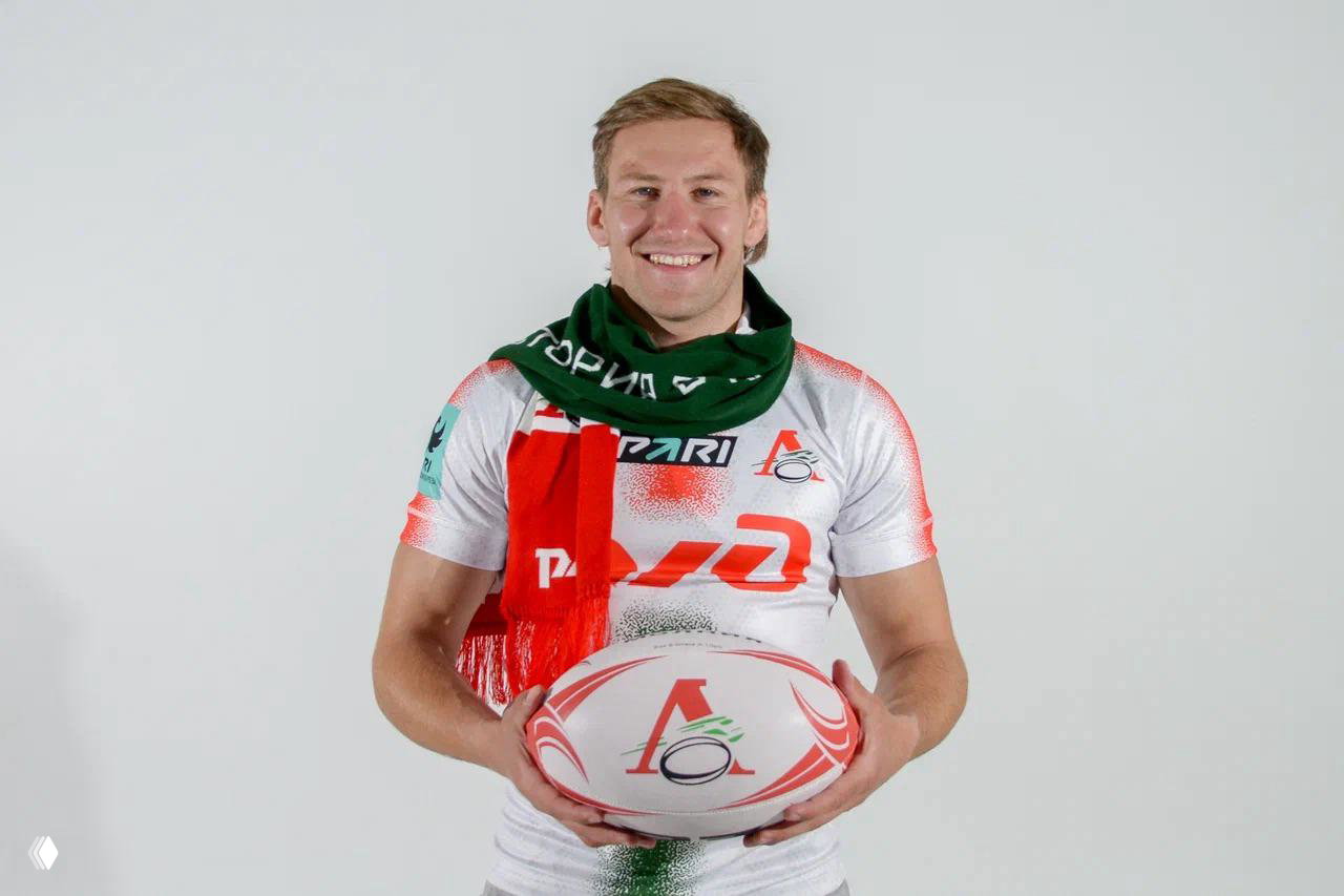 Игрок держит регбийный мяч и улыбается, на нём видно фирменные цвета и логотипы — пример брендированного мерча для клуба.