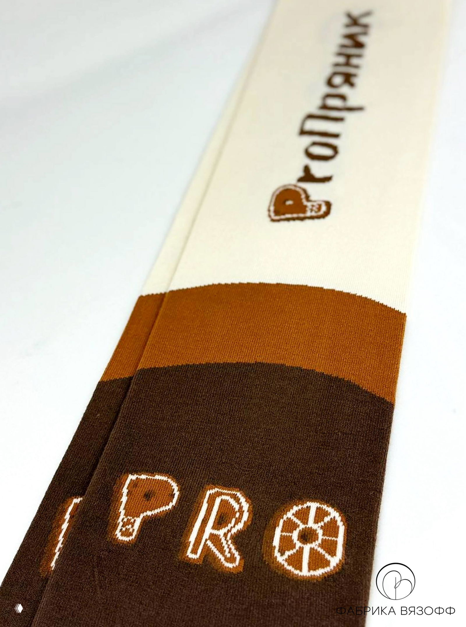 Длинный фрагмент шарфа в перспективе: плавные переходы коричневых полос, ровный трикотаж и частично виден логотип «ФАБРИКА ВЯЗОФФ» в углу изображения.
