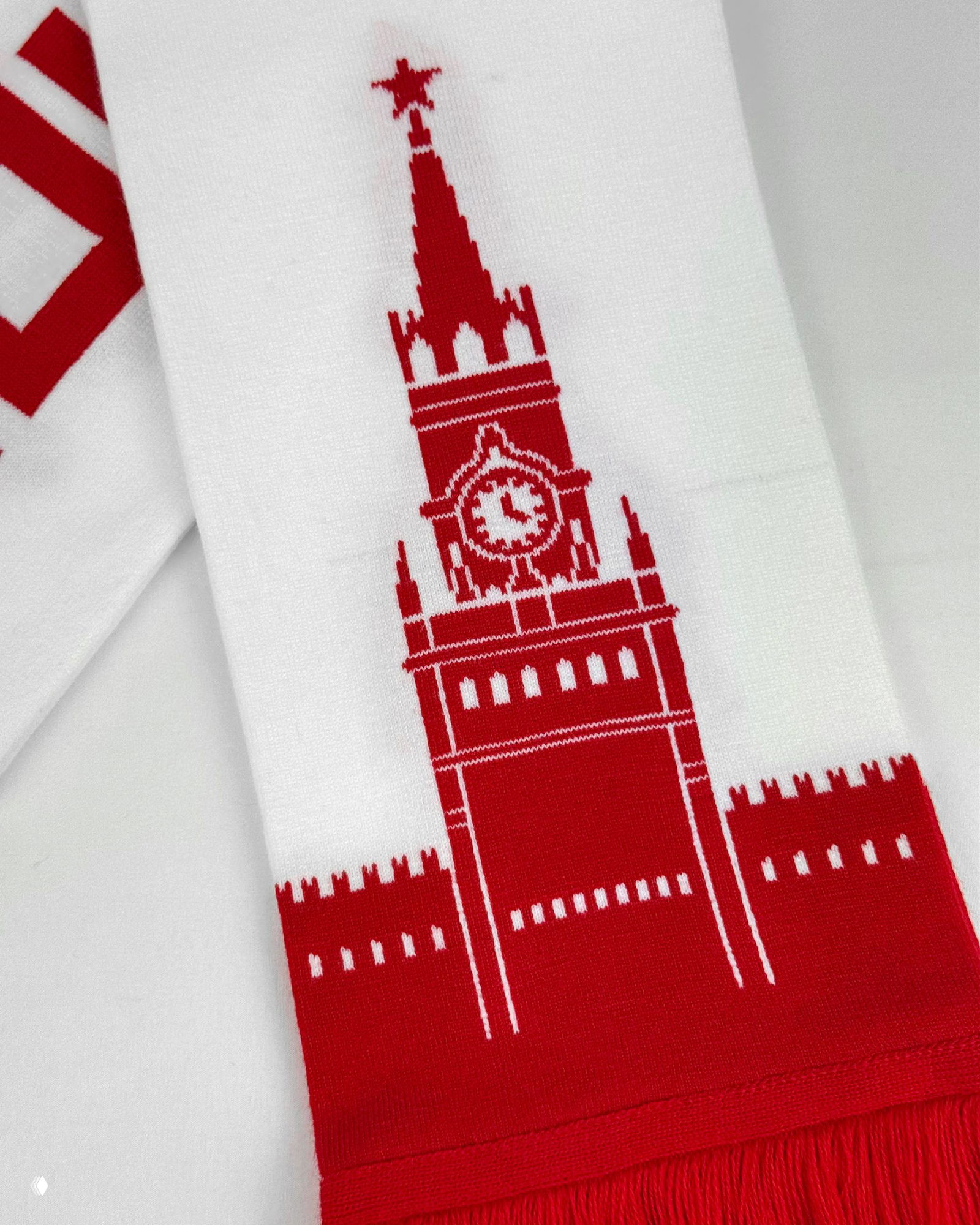 Крупный план вывязанного узора со Спасской башней в красном на белом фоне: видна текстура нитей, рисунок и бахрома шарфа.