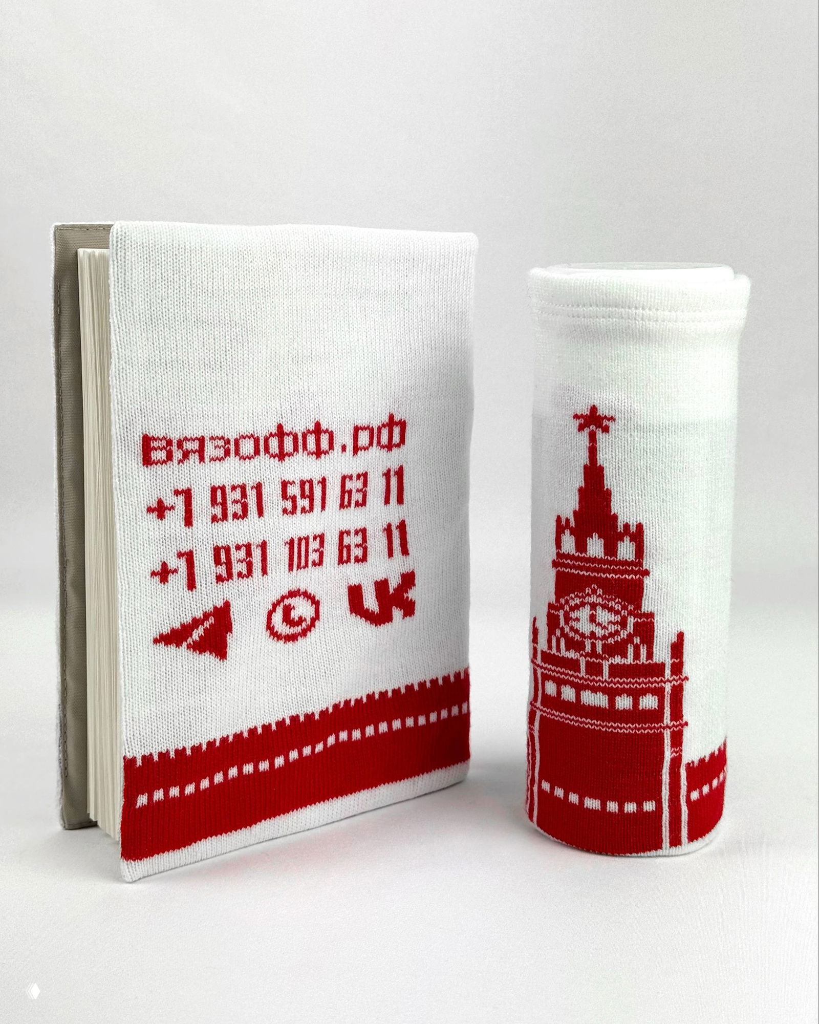 Обложка ежедневника с вывязанными контактами компании и рядом чехол для термоса: белая основа и красная вязка с логотипом и номерами.