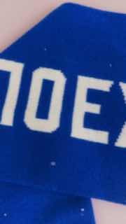 Крупный план синего вязаного полотна шарфа с белыми буквами, видно фрагмент надписи «ПОЕХ…» и структуру пряжи на крупном масштабе.