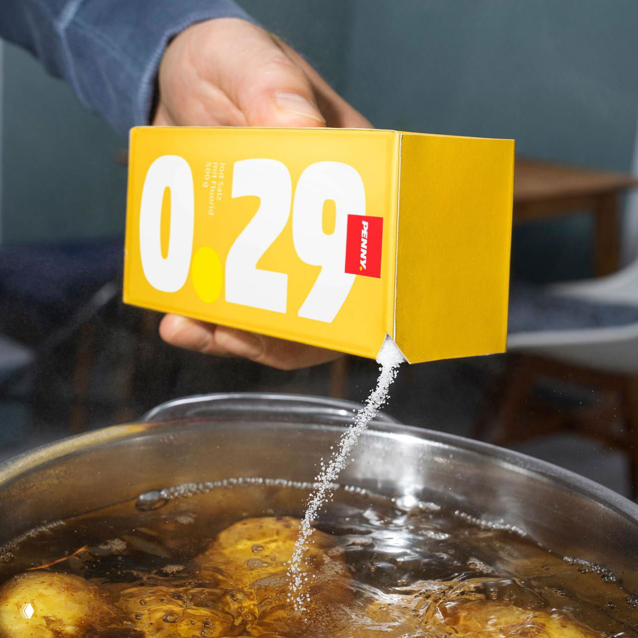 Человек на кухне с коробкой в желтой упаковке, из которой сыпется соль или продукт в кастрюлю, крупная цена 0.29 напечатана на коробке.