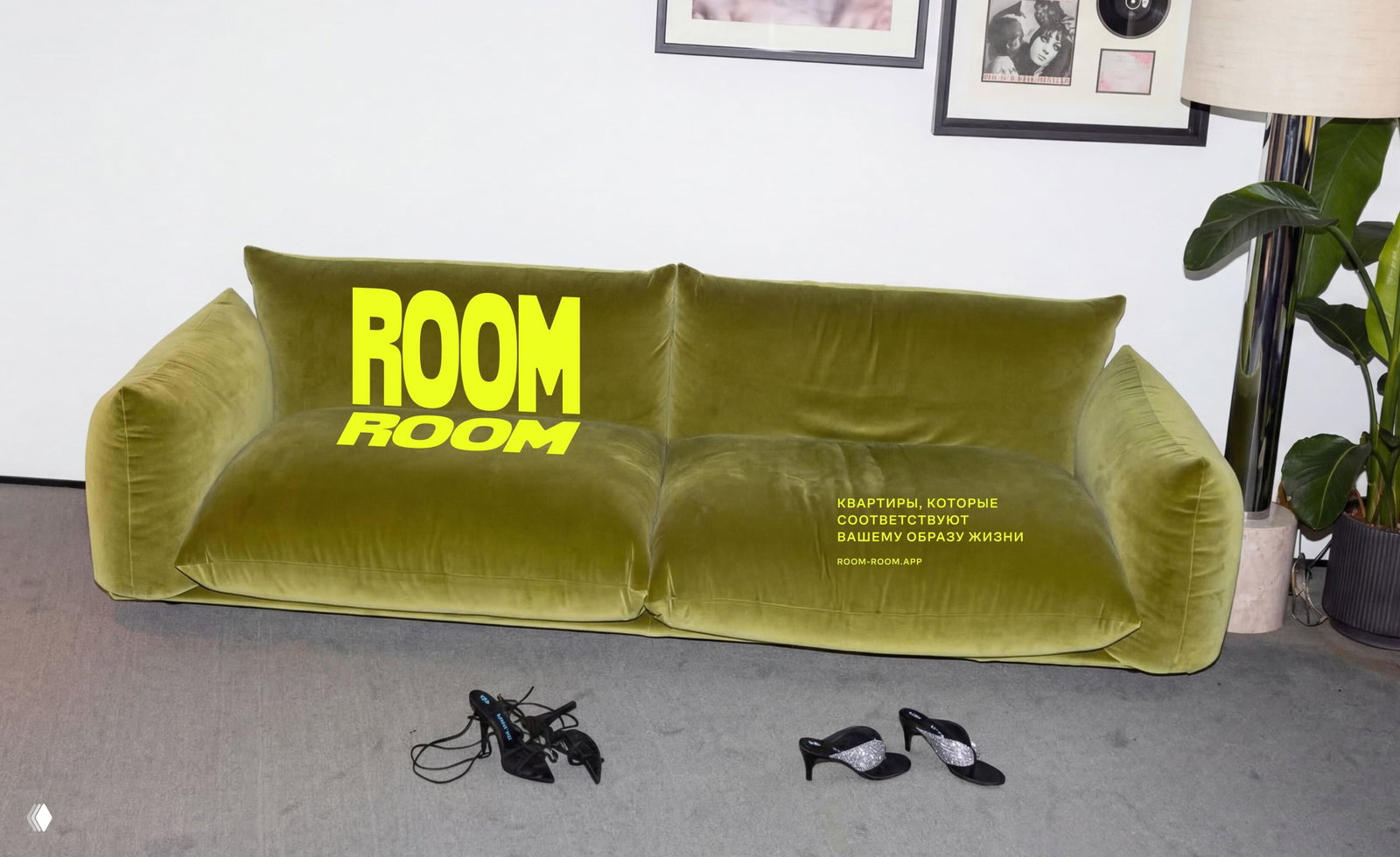 Интерьерная фотография: оливковый диван с крупным жёлтым логотипом ROOM на поверхности и небольшими предметами интерьера в кадре.