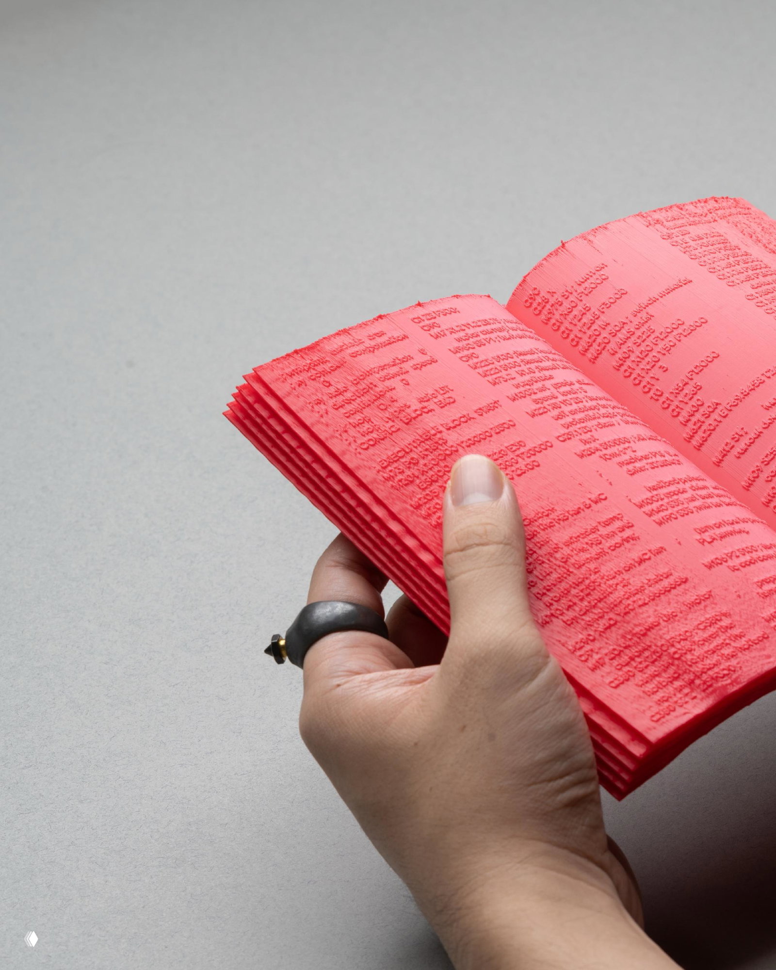Рука держит красную 3D-печатную книгу крупным планом; видны текстуры и рельеф страниц, корешок и декоративные элементы переплёта на светлом студийном фоне.