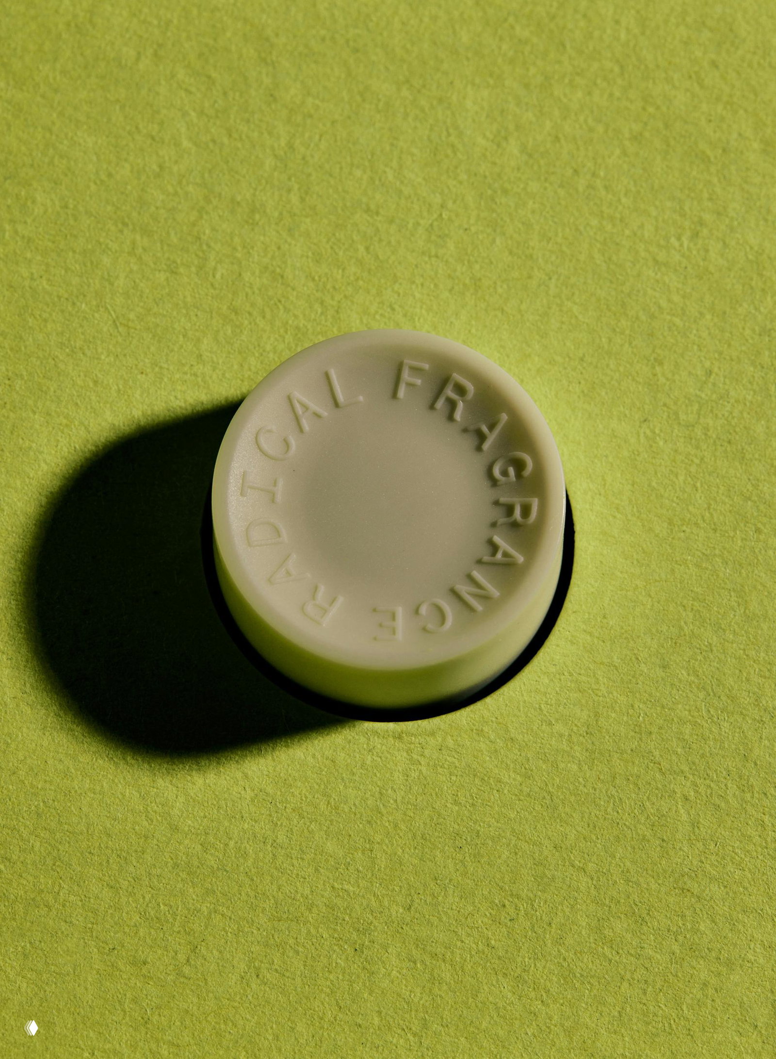 Крупный план круглой матовой крышки флакона с рельефной надписью и глубокой тенью на светло‑зелёном фоне.