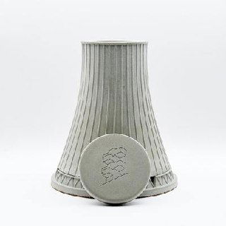 Конусообразная бетонная миниатюра с круглым диском-логотипом на переднем плане: фактура бетона и чистая белая подложка.