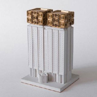 Миниатюра многоэтажного здания с декоративными золотистыми верхними блоками: сочетание бетона и металлических вставок.