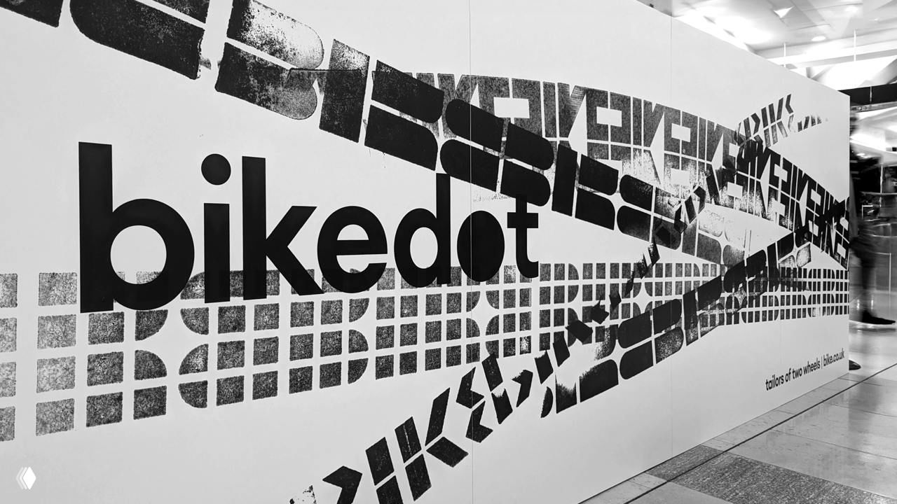 Стена с крупной инсталляцией bikedot: логотип и динамичные следы протектора, нанесённые полосами, монохромная уличная графика в интерьере.