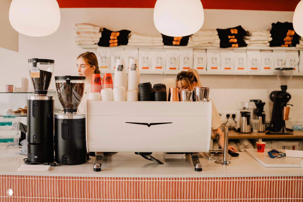 Вид внутренней стойки кафе: кофейное оборудование, стаканы с логотипом Drip и аккуратно уложенные пакеты на полках — интерьерный кадр брендинга.