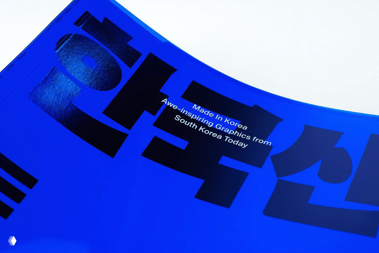 Близкий ракурс прозрачной синей обложки с блестящей тиснёной чёрной типографикой и отражениями света, подчёркивающий текстуру материала обложки.