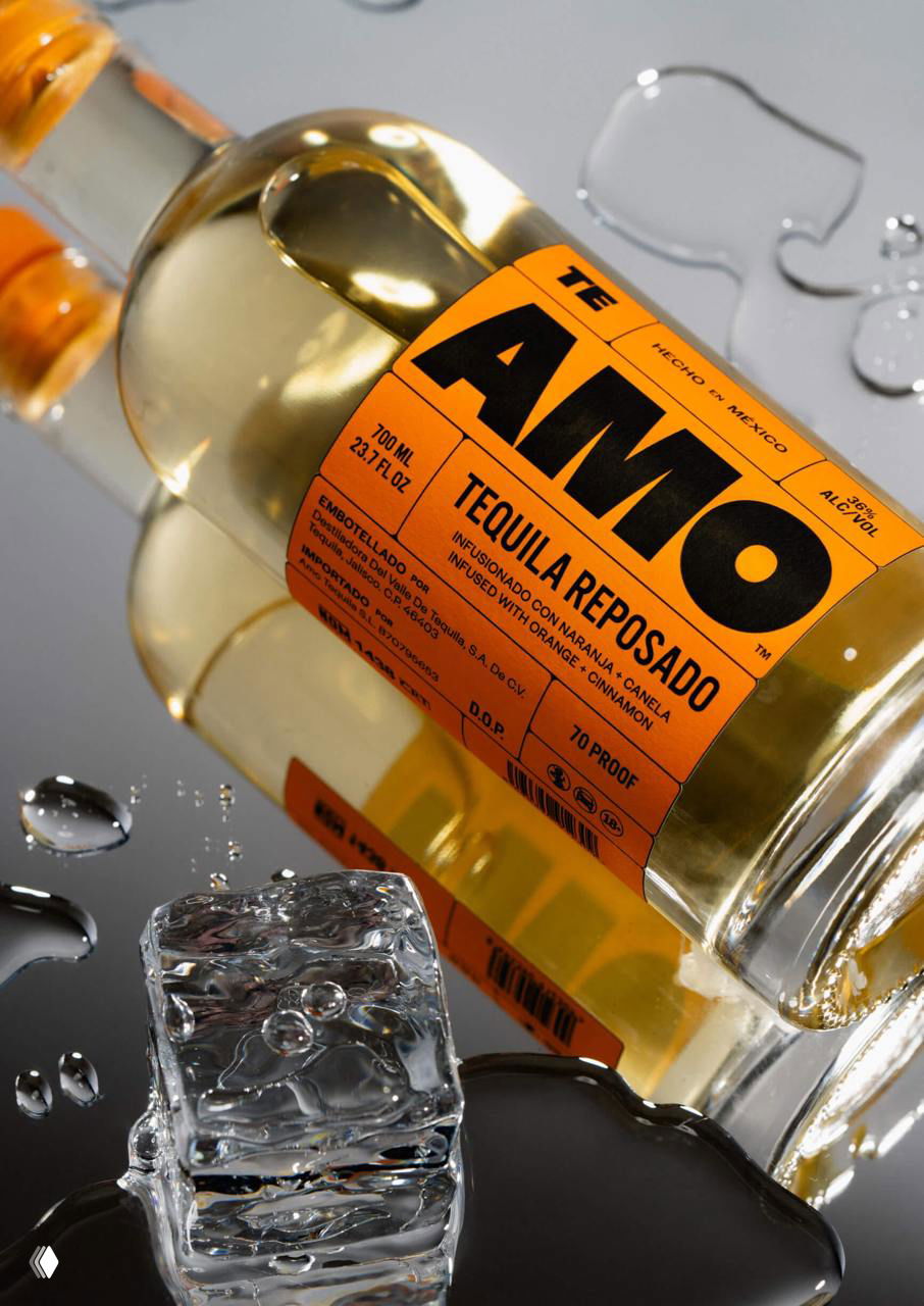 Крупный план бутылки текилы Amo, лежащей на зеркальной поверхности, видно крупное этикетирование и кусок льда в переднем плане