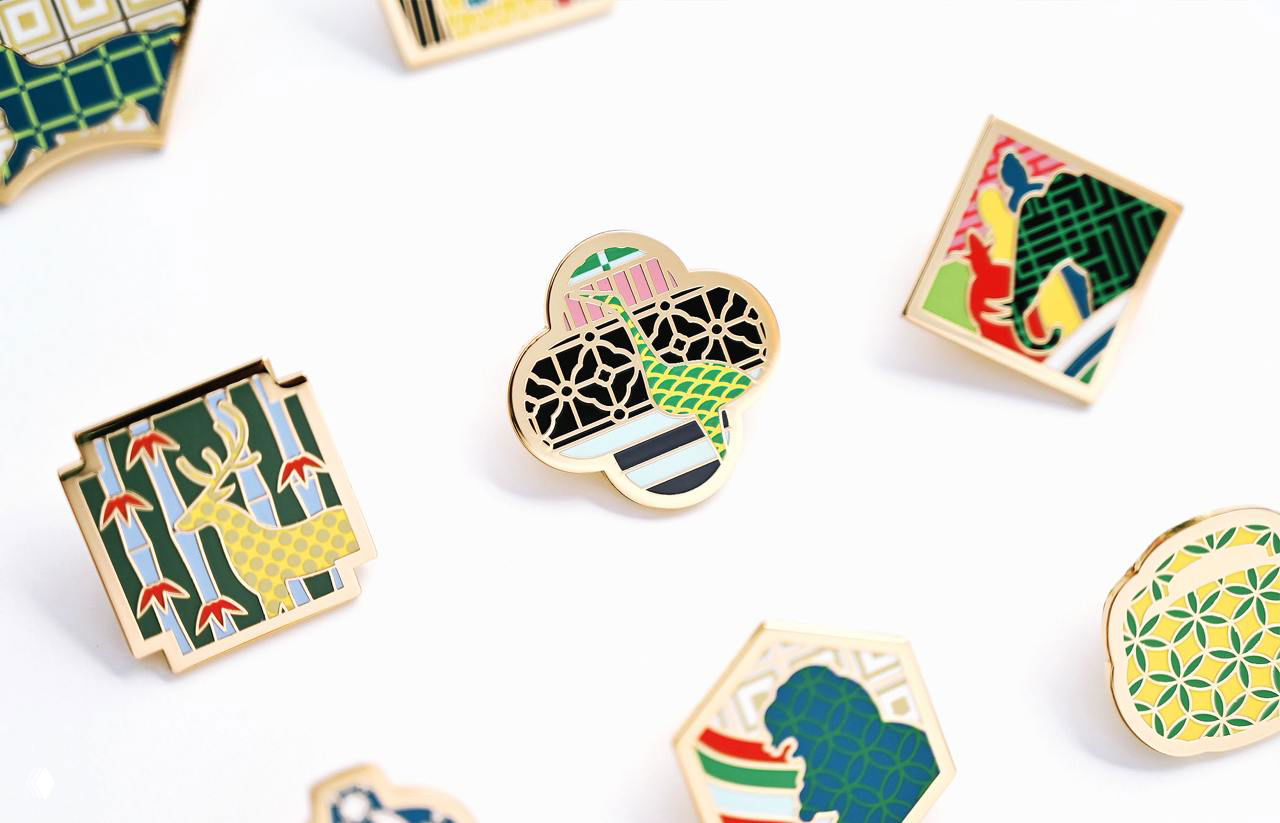 Набор металлических значков и пинов с миниатюрными узорами и яркими цветами, выполненных по мотивам росписей и архитектурных элементов музея
