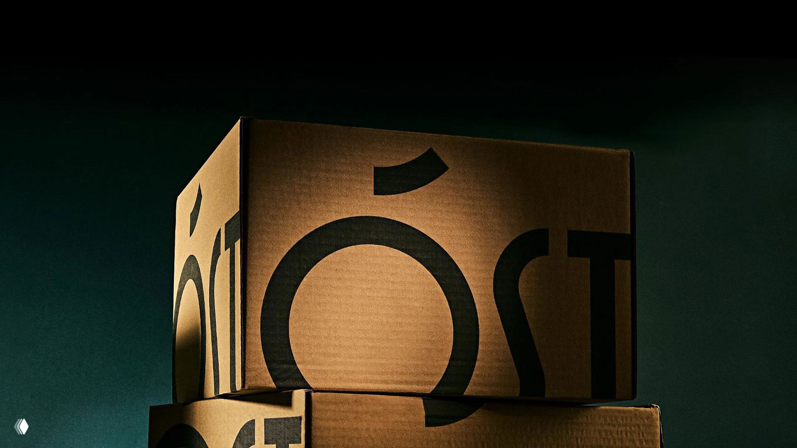 Картонные коробки с крупным чёрным логотипом ÓST, сложенные стопкой; фотография демонстрирует упаковочный макет и масштаб марки.