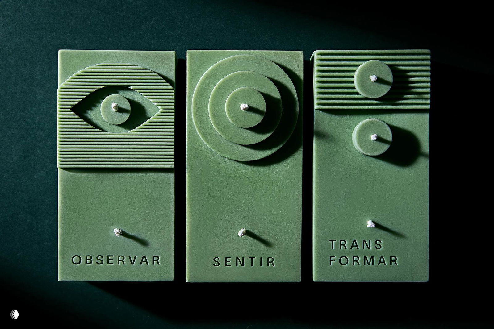 Три зелёные рельефные свечи с геометрическими круглыми мотивами и подписями OBSERVAR, SENTIR, TRANSFORMAR на тёмном фоне.