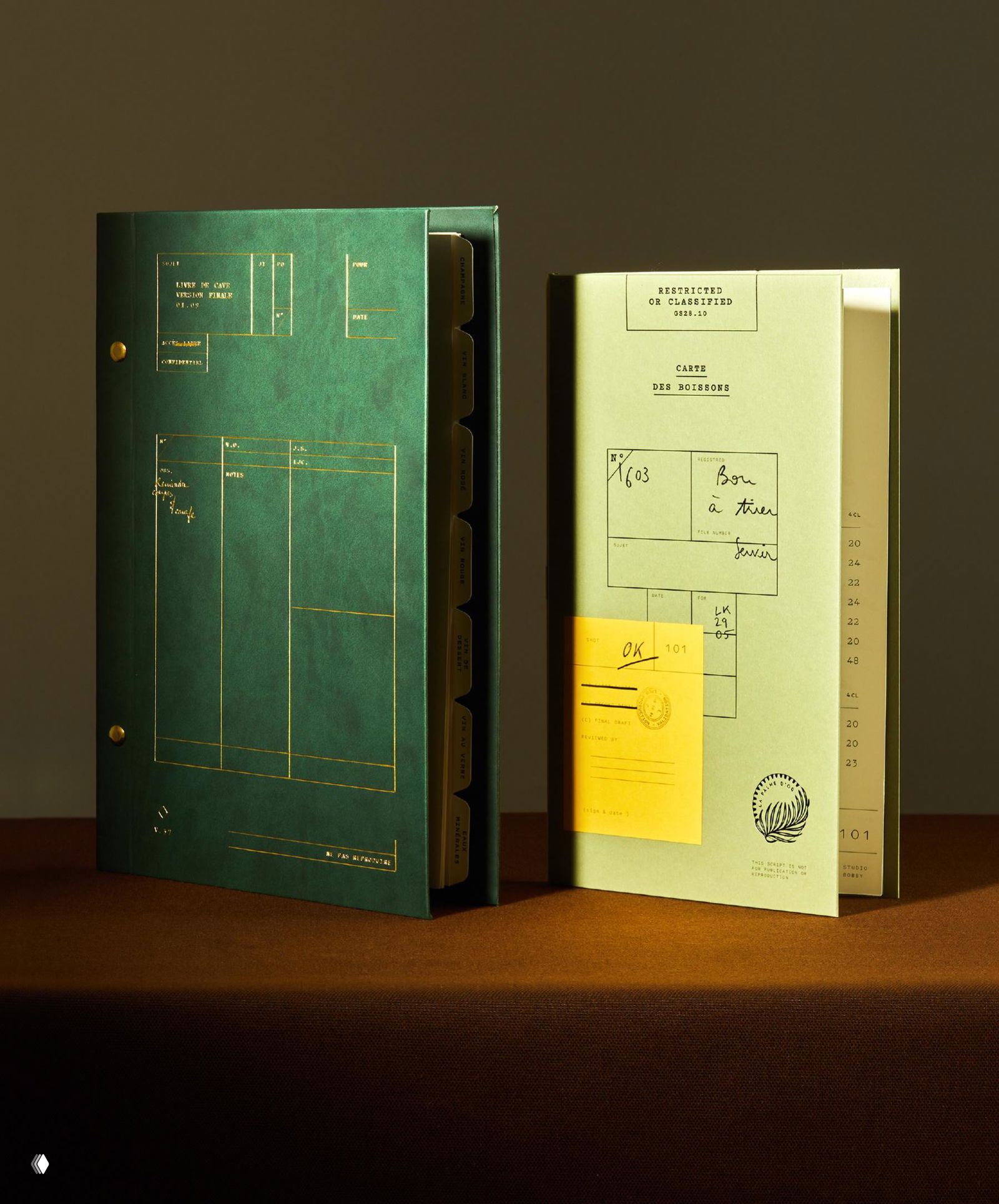 Два раскрытых буклета La Palme d’Or: тёмно-зелёная папка с золотыми линиями и светло-зелёное меню с пометками, сдержанная типографика на фоновой поверхности.