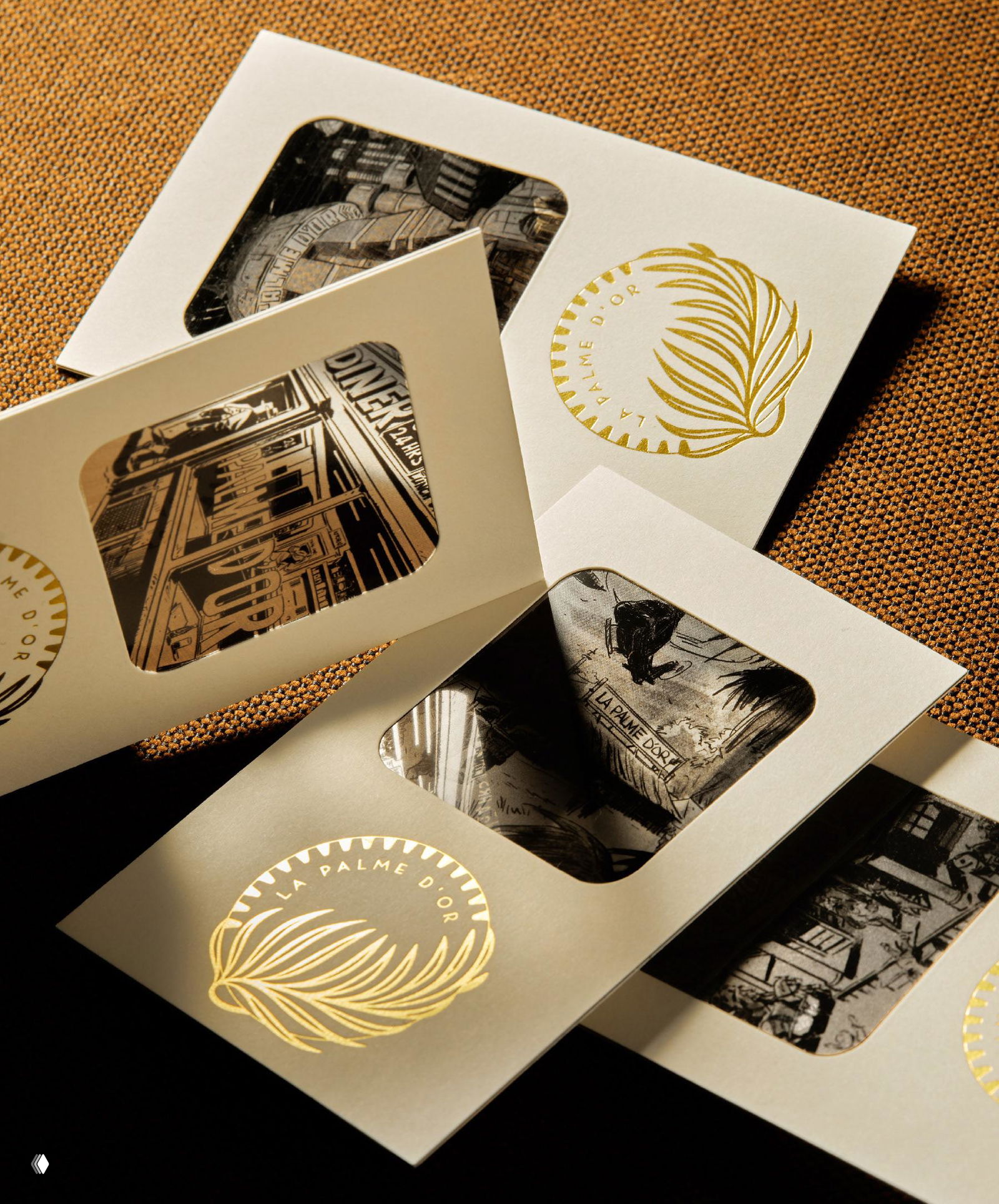 Набор карточек с вырубными окнами и золотым логотипом La Palme d’Or; контраст монохромных иллюстраций в окне и тёплый текстильный фон.