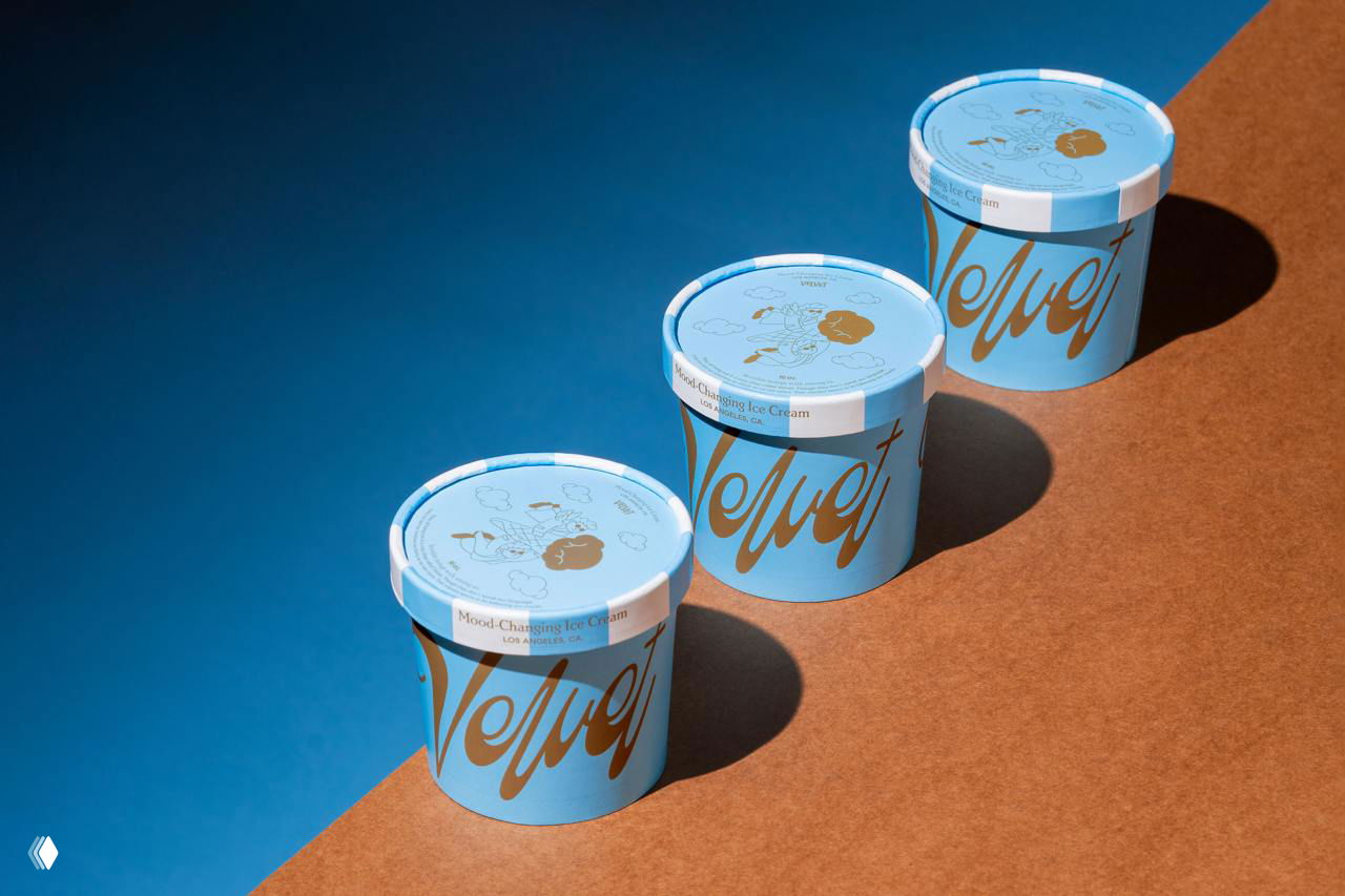 Три бумажных стаканчика мороженого Velvet голубого цвета с крупным золотым логотипом; студийная съемка подчёркивает упаковочную графику и тени.
