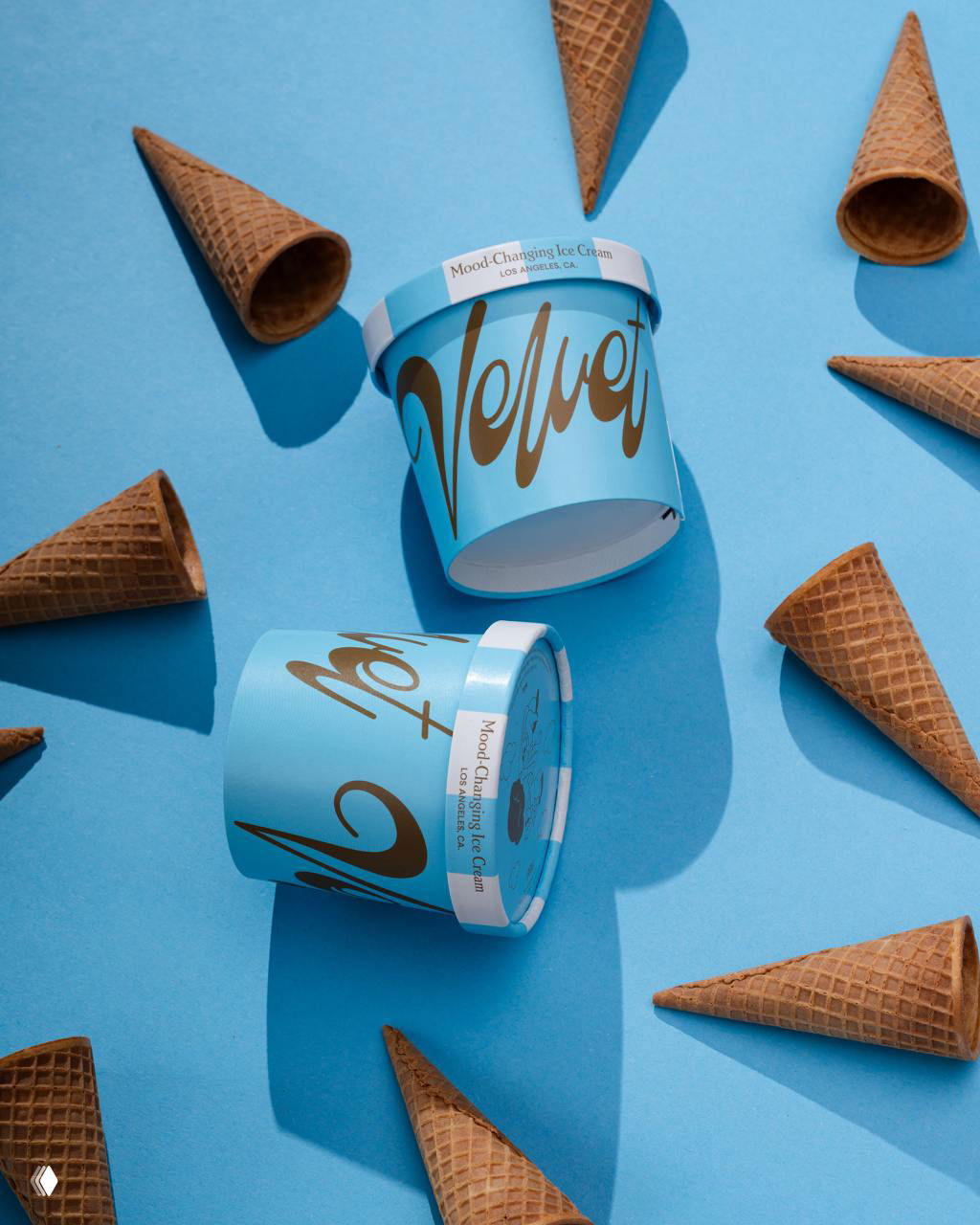 Креативная композиция: коричневые вафельные рожки вокруг баночек Velvet на голубом фоне; рекламная фотосессия упаковки продукта.