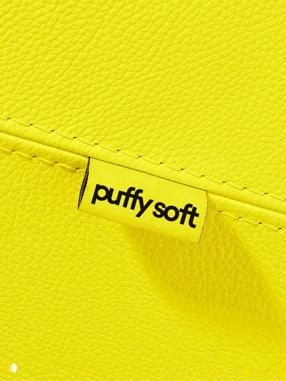 Крупный план жёлтой текстильной бирки с логотипом «puffy soft» на фактурной коже — деталь упаковки и элемент фирменного стиля, подчёркивающая качество материалов.
