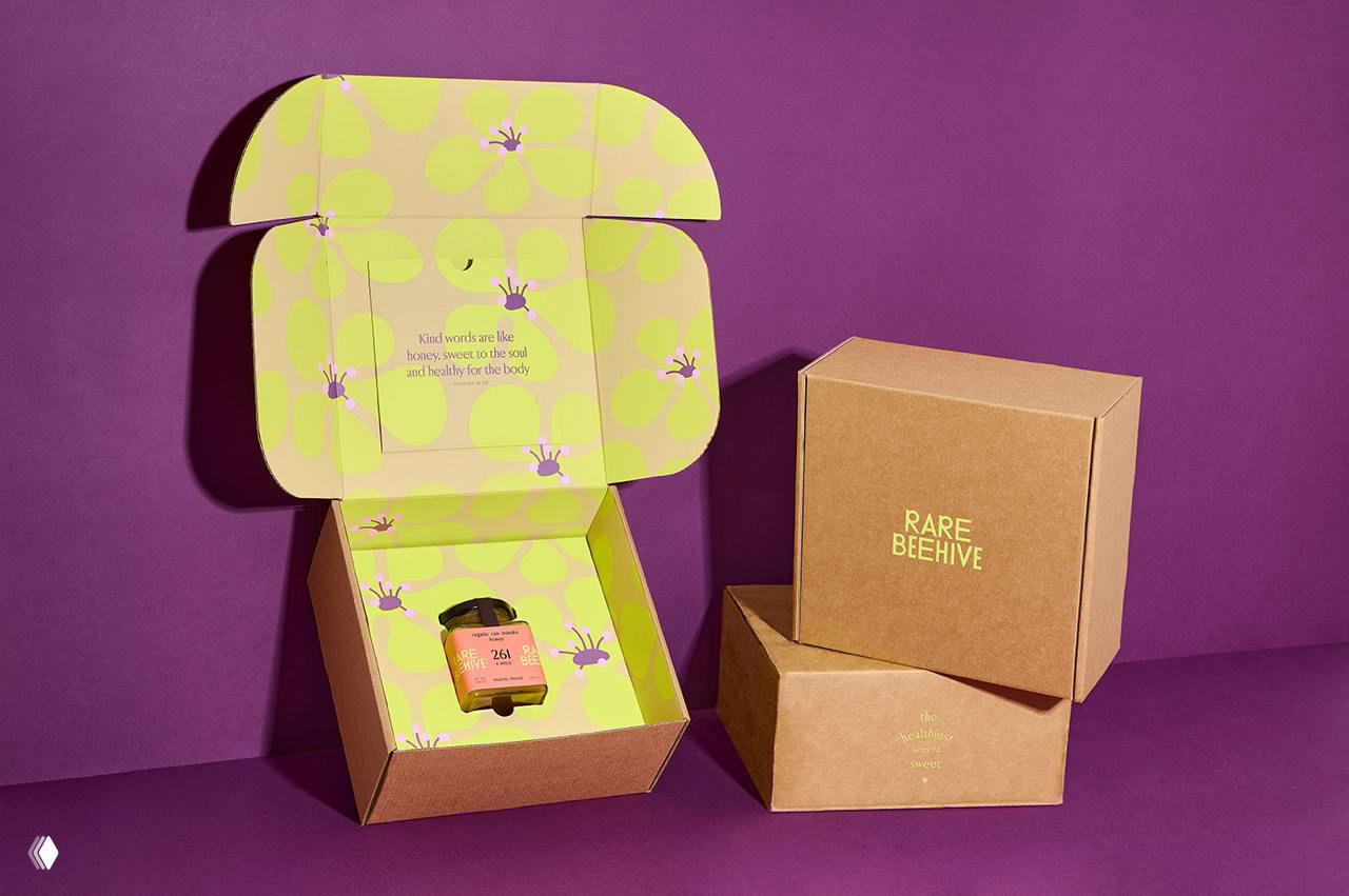 Открытая подарочная коробка с интерьером в лимонных тонах и цветочными иллюстрациями, внутри аккуратно размещена маленькая баночка мёда Rare Beehive.